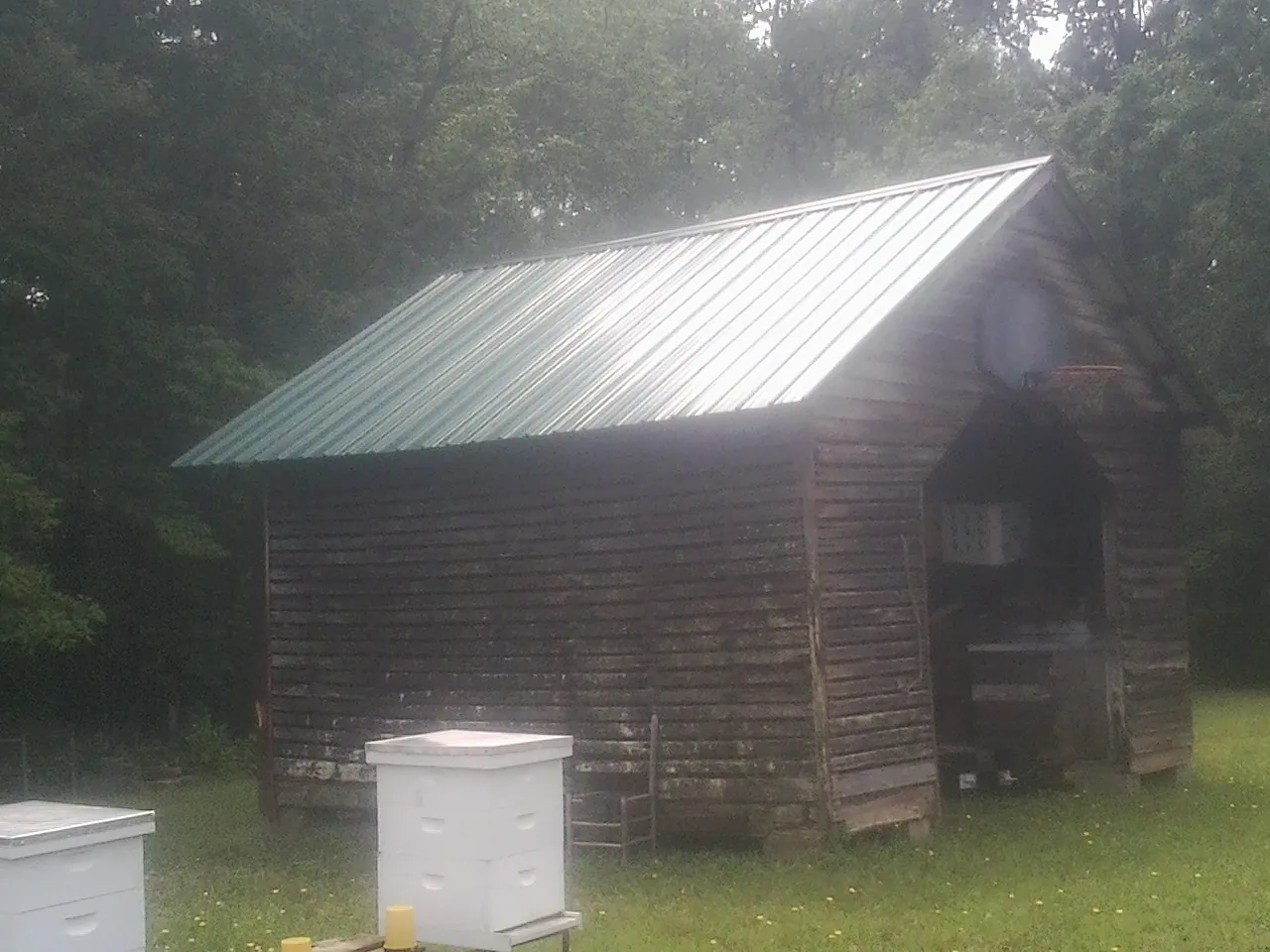 Green metal roof on a weathered barn beside stacked beehives in American Fork