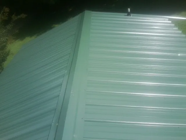 New green metal panels meeting at the ridge of a roof — Flat Roof Repair work by our crew in American Fork